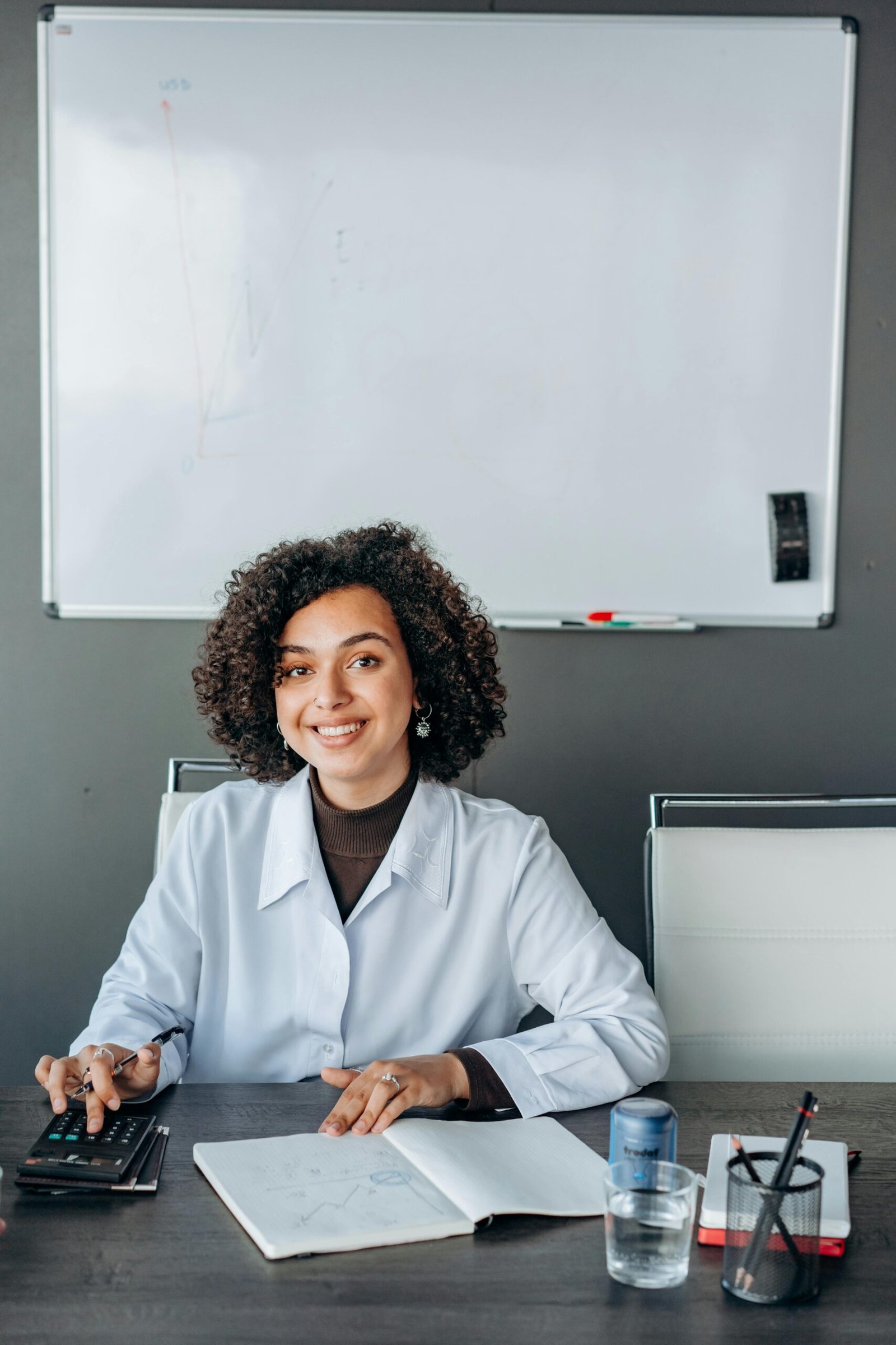 Smiling woman in office working with papers and calculator.